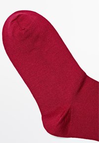 Rød sok lavet af glat, strækbart materiale, med en rund tå, ribbet kant og sømløst design.