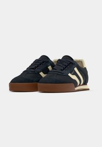 Στιλάτα ναυτικά μπλε σουέτ sneakers με εκρού λεπτομέρειες, σχ εδιασμό δέσιμου με κορδόνια και καφέ καουτσούκ σόλα με υφή. Διαθέτουν δύο πλευρικές ρίγες και μαξιλαρωμένη γλώσσα.