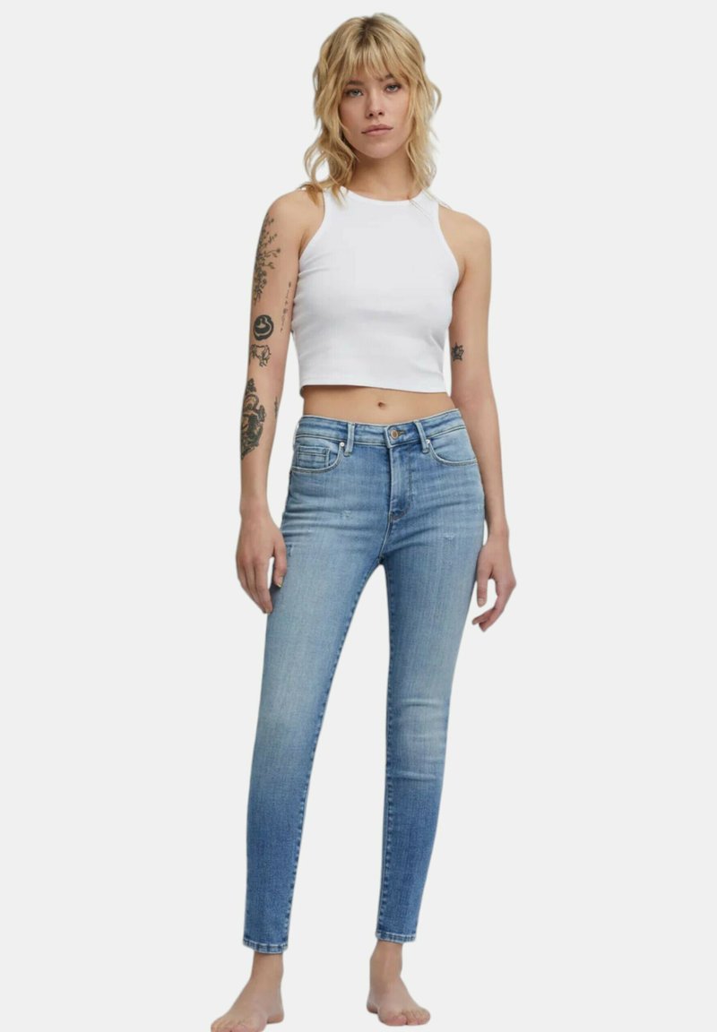 Jeans skinny azzurri chiari con un design sbiadito, stile a cinque tasche e vita a media altezza, abbinati a un top corto bianco.