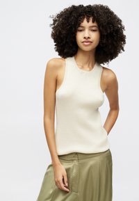 Knit sleeveless top in cream color with a fitted design, featuring a round neckline and ribbed accents, paired with olive green silky pants.