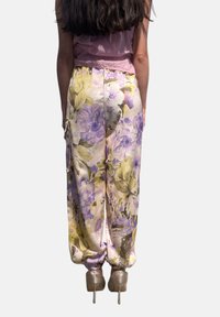 Pantaloni floreali in tonalità pastello chiare con motivi viola e verdi, caratterizzati da una vestibilità ampia, caviglie arricciate e una consistenza liscia simile alla seta.