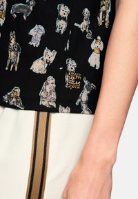 Black shirt featuring a variety of dog illustrations in light colors. Includes a small branded patch with a leopard print design.