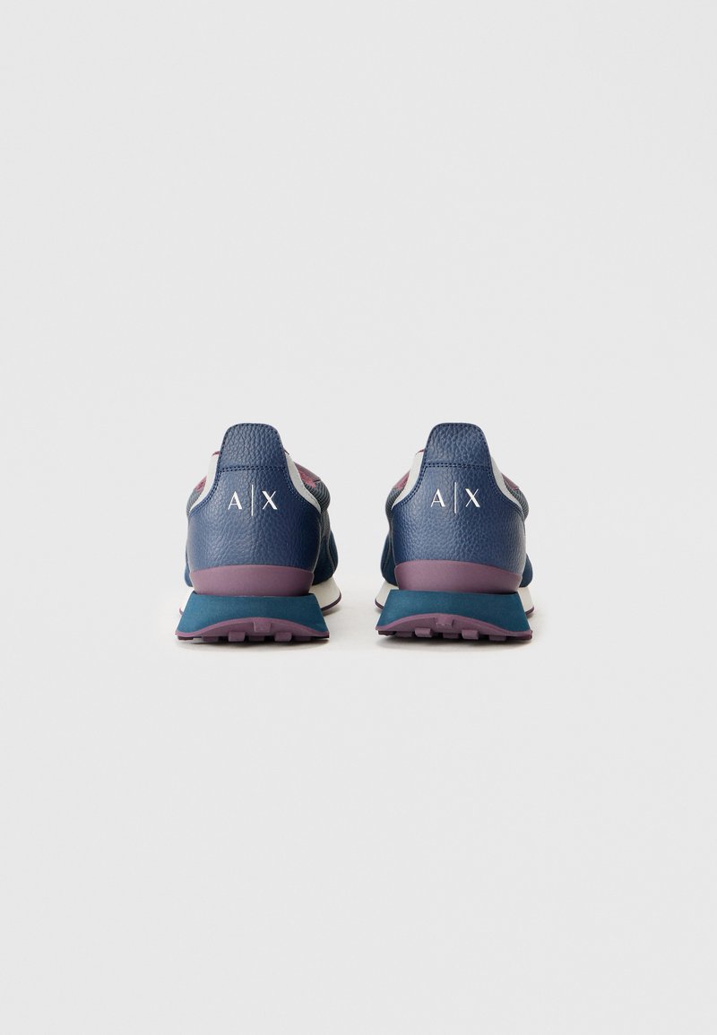 Une paire de baskets de sport bleues et violettes avec des logos blancs "A|X" à l'arrière, présentée de dos sur un fond blanc uni.