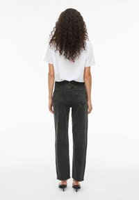 Crne traperice visokog struka ravnog kroja s izblijedjelim završetkom, s stražnjim džepovima i skraćenim rubom, u kombinaciji s bijelom majicom.