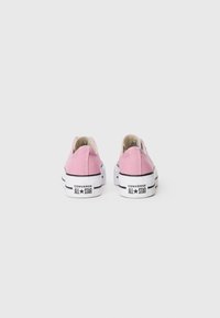 Pink canvas low-top sneakers with white rubber soles, black accents, and signature logo on the heel. Light stitching details on the sides.