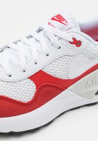 Sneaker Nike Air Max con tomaia in mesh bianco, accenti in suede rosso, lacci bianchi e un importante contrafforte posteriore grigio con logo "AIR".