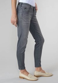 Šedé slim-fit džíny vyrobené z denimu, s jemným vyblednutím a designem s pěti kapsami. Nosí se s světle zbarvenými mokasíny.