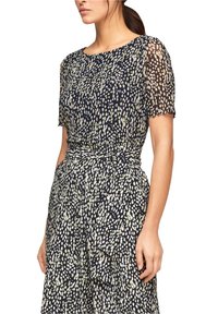 Marinblå klänning med ett ljust fläckigt mönster, korta genomskinliga ärmar, en rynkad midja och en flödande kjol med volanger.