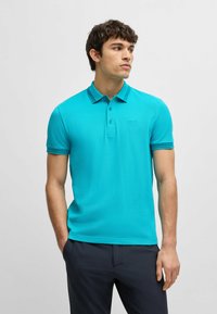 Turkos polo skjorta med klassisk krage, korta ärmar och subtil broderad logotyp. Slinky tyg med en figurnära silhuett.