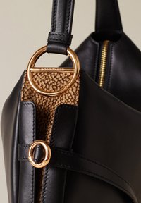 Borsa a tracolla nera in pelle con una decorazione circolare in metallo dorato e un pannello marrone texturizzato. Chiusura con zip su un lato.