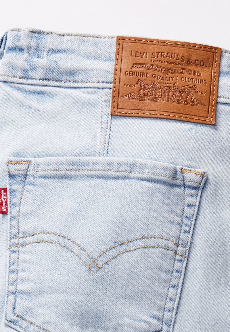Hellblaue Jeans aus Denim verfügen über ein Leder-Logo-Patch, eine hintere Tasche mit markanter Naht und ein rotes Etikett an der linken Seite.