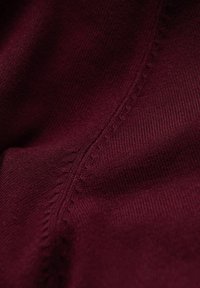 Tissu bordeaux présentant un tissage texturé avec des coutures et des détails de couture visibles, soulignant sa surface lisse et sa couleur riche.