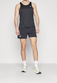 Svart ärmlös tanktop med rund halsringning, kombinerad med mörka shorts med en logotyp. Denna outfit kompletteras av ljusa sneakers.