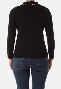 Maglione nero a coste con un collo a pois, maniche lunghe e una silhouette aderente, abbinato a jeans blu con tasche posteriori.