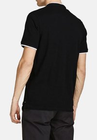 Sort polo skjorte med klassisk pasform. Har hvide detaljer på kraven og ærmeenderne. Glat bomuldsstof med en subtil tekstur.