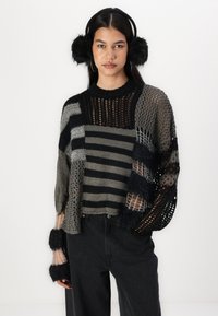 Sweater de crochê em materiais mistos com listras pretas e cinzas, desenho de malha aberta e detalhes de pelagem sintética nos punhos das mangas. Jeans pretos.