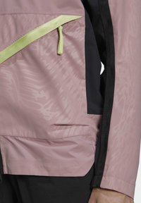 Vattentät jacka i ljusrosa och svart, med en texturerad mönster, limegrön dragkedjedetalj och sidoficka.