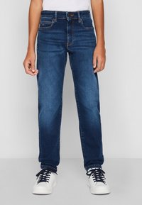 Jeans de denim azul oscuro con corte recto, que cuentan con cinco bolsillos, cierre de botón y costuras en contraste. Combinados con zapatillas blancas.