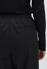 Pantalons noirs avec une coupe décontractée, dotés d'une taille élastique, de deux poches incrustées et d'une texture lisse. Le tissu semble léger.