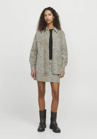 Completo giacca e gonna in stampa leopardata nei toni beige e marrone, caratterizzato da una vestibilità ampia, chiusura con bottoni e abbinato a stivali neri alla caviglia.