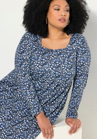 Sukienka w kwiaty z ciemnoniebieską bazą, na której widnieją jasnoniebieskie i białe kwiaty. Długie rękawy i kwadratowy dekolt. Miękka, strukturalna tkanina.