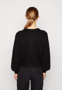 Musta neulepaita, jossa pyöreä pääntie, roikkuvat hihat, resoriset hihansuut ja helma. Yhdistetty tummiin farkkuihin, nähtynä selkäpuolelta.