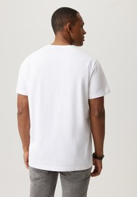 Biała bawełniana koszulka z krótkim rękawem o klasycznym okrągłym dekolcie i luźnym kroju, w zestawie z jasnoszarymi dżinsami.