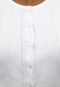 Λευκό πουκάμισο με κάθετες υφασμάτινες ρίγες, κοντινή λήψη εστιασμένη στο πάνω μισό με πέντε ορατά κουμπιά κλειστά.