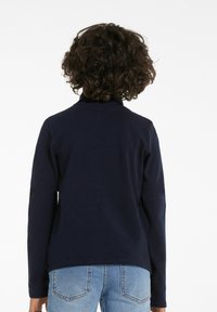 Marineblaues Langarmoberteil mit hohem Kragen, das eine glatte Textur und ein schlichtes Design aufweist. Kombiniert mit hellblauen Jeans.