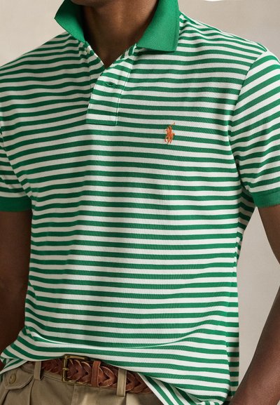 Πράσινο και λευκό ριγέ πόλο πουκάμισο με πράσινο γιακά και μικρό κεντητό πορτοκαλί λογότυπο, φορεμένο με μπεζ παντελόνι και πλεξούδα καφέ ζώνη.