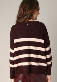 Pull rayé bordeaux et crème avec une coupe ample, fabriqué à partir d'un matériau doux, présentant un col rond et un petit accent doré à l'arrière.