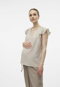 Beige graviditetstopp med volangärmar, V-ringning, textilier med struktur och sidoknyten för justerbar passform. Matchas med beige vida byxor.
