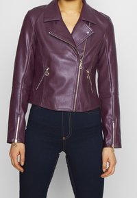 Veste de moto en cuir bordeaux avec des zips argentés, design cropped, col à pression et poches zippées. Texture lisse et coupe ajustée.
