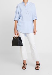 Camicia azzurra chiara con maniche arrotolate, abbinata a pantaloni bianchi a vita alta e borsa nera con manici in legno. Sandali neri con cinturini.