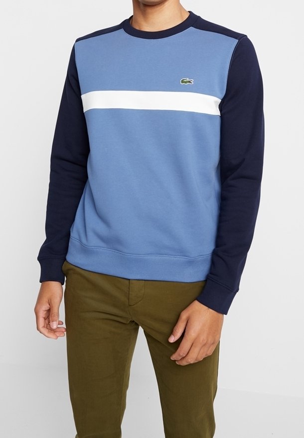 Homme portant un sweat-shirt colorblock à manches longues avec des panneaux bleus et bleu marine et un pantalon vert olive.