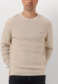 Maglione lavorato a maglia beige con un motivo strutturato, scollatura a girocollo, polsini e orlo a costine. Presenta un piccolo logo ricamato sul lato sinistro del petto.