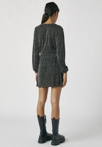 Robe noire avec un motif à pois, manches longues, taille élastique et jupe courte. Portée avec des bottes noires jusqu'aux genoux. Texture lisse.