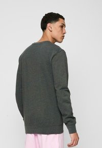 Sweatshirt gri cu mâneci lungi, de tip crew neckline, și tivuri ribbate. Prezintă un material texturat cu o variație de culoare subtilă.