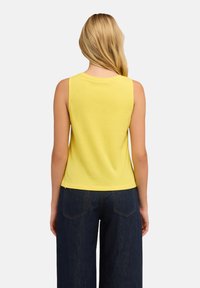 Top giallo senza maniche in cotone con scollatura rotonda. La parte posteriore è liscia e si abbina a pantaloni a gamba larga blu scuro con tasche a toppa.