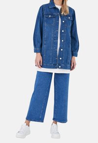 Sininen farkkutakki pitkillä hihoilla, etutaskuilla ja napillisesti suljettava, yhdistetty leveälahkeisiin farkkuihin ja valkoisiin tennareihin. Yksinkertainen malli.