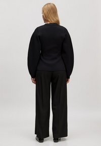 Zwarte trui met oversized pofmouwen, gecombineerd met zwarte wijde broek. Glad textuur, eenvoudig ontwerp en geen zichtbare hardware.
