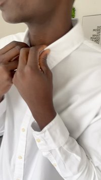 Uomo che sistema il colletto di una camicia bianca con bottoni all'interno, con un poster motivazionale parzialmente visibile sullo sfondo.
