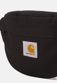 Borsa a sacchetto in tessuto nero di forma rotonda, con un'etichetta a logo bianca con un design arancione e chiusura con cerniera.