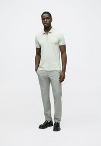 Lysegrå poloshirt med lynlåslukning ved kraven, kombineret med tilpassede lysegrå bukser og sorte sko. Glat stof med en subtil tekstur.