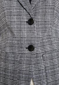 Zwart-wit geruite blazer met een textuurstof, voorzien van twee zwarte knopen en een gekartelde revers.