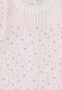 Prenda de color rosa claro con estampado floral y pequeños puntos negros. Presenta un escote con volantes y pliegues verticales en la parte superior.