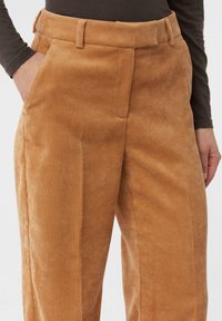 Spodnie sztruksowe w ciepłym odcieniu beżu, z pionową prążkowaną teksturą, prostym krojem, bocznymi kieszeniami i paskiem w talii.