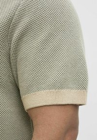 Gebreid shirt met korte mouwen in lichtgroen met een gestructureerd patroon. Ribbelige beige boorden en kraag bieden contrast met het ontwerp van het lichaam.