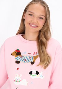 Sudadera rosa con motivos de perros bordados y acentos y texturas coloridos. Los patrones destacados incluyen rayas y detalles florales.
