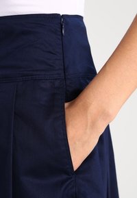 Navyblauwe rok met een zijzak en ritssluiting. De stof lijkt glad met een lichte glans en is ontworpen met een getailleerde pasvorm.